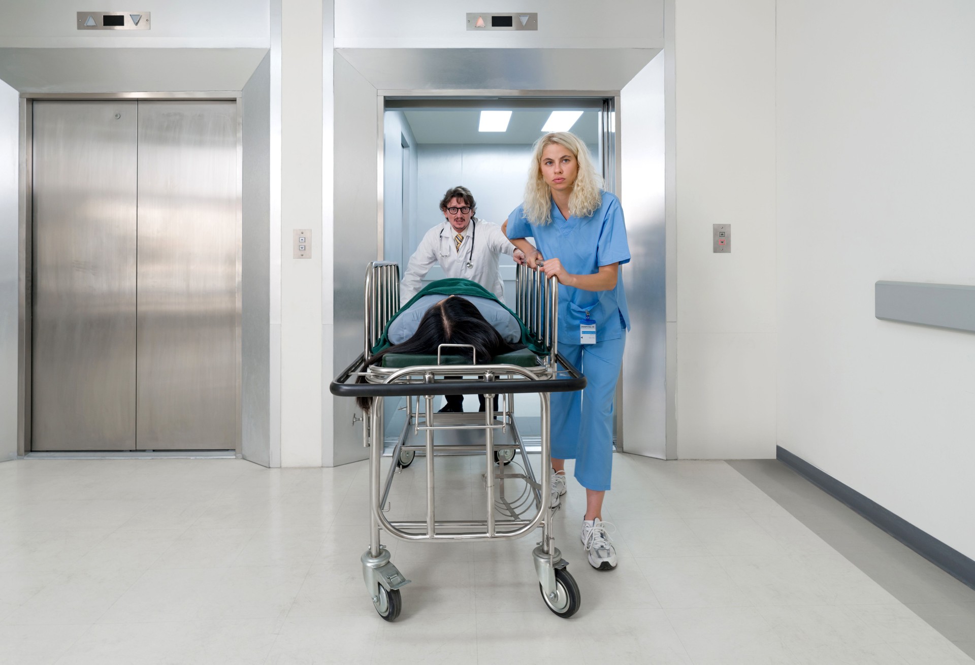 A nurse and doctor in propels a wheeled stretcher, carrying a patient out of the elevator to the emergency room of the hospital. A nurse and doctor in propels a wheeled stretcher, carrying a patient out of the elevator to the emergency room of the hospital.